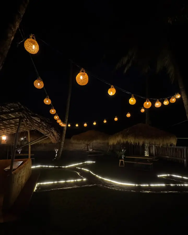 Amber rattan globes hanging over the garden, thatched cabanas and a lit path across the lawn